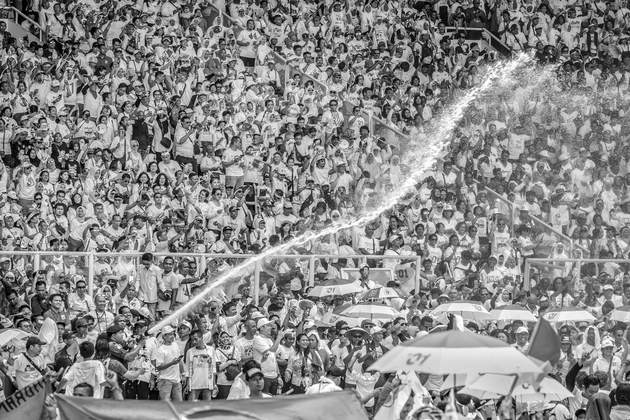 Indonesia -   A fireman spray water to keep supporters of...