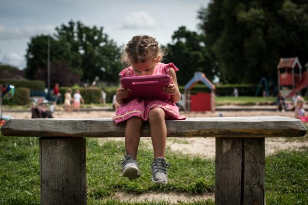 Tessa, 2 yo, watching a tablet in a playground.&nbsp; I happened to witness a similar situation and I re-created it for this portrait.&nbsp; According to research, higher levels of screen use in children and adolescents is associated with reduced physical activity, increased risk of depression, and lower wellbeing. United Kingdom, 2019 &copy;ChiaraCeolin