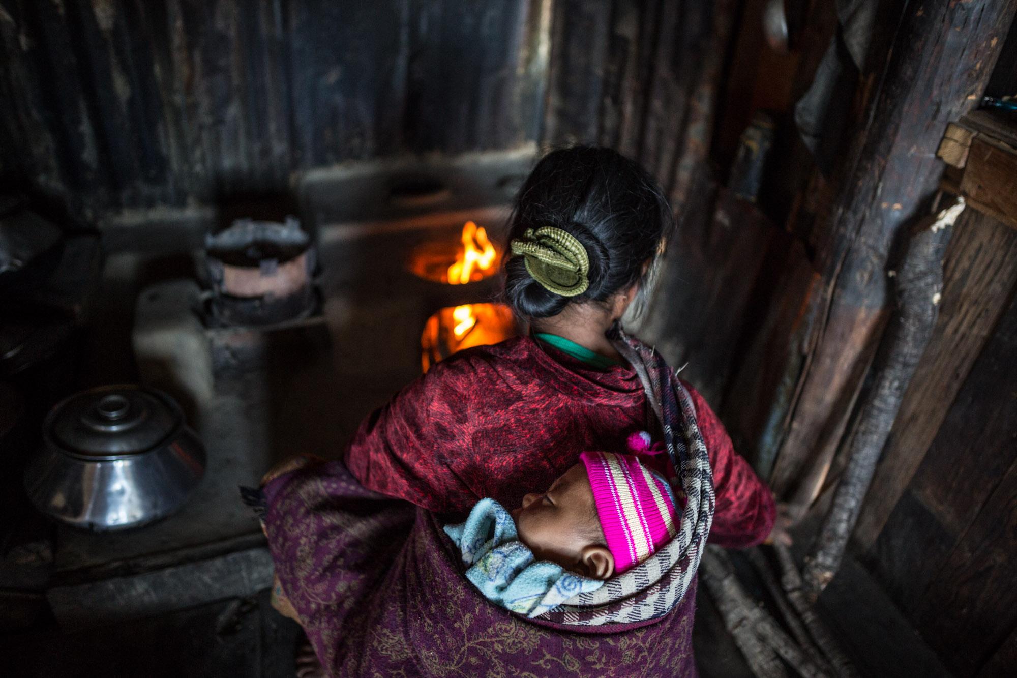 NGO - A mother cooks with her baby strapped to her back at her...
