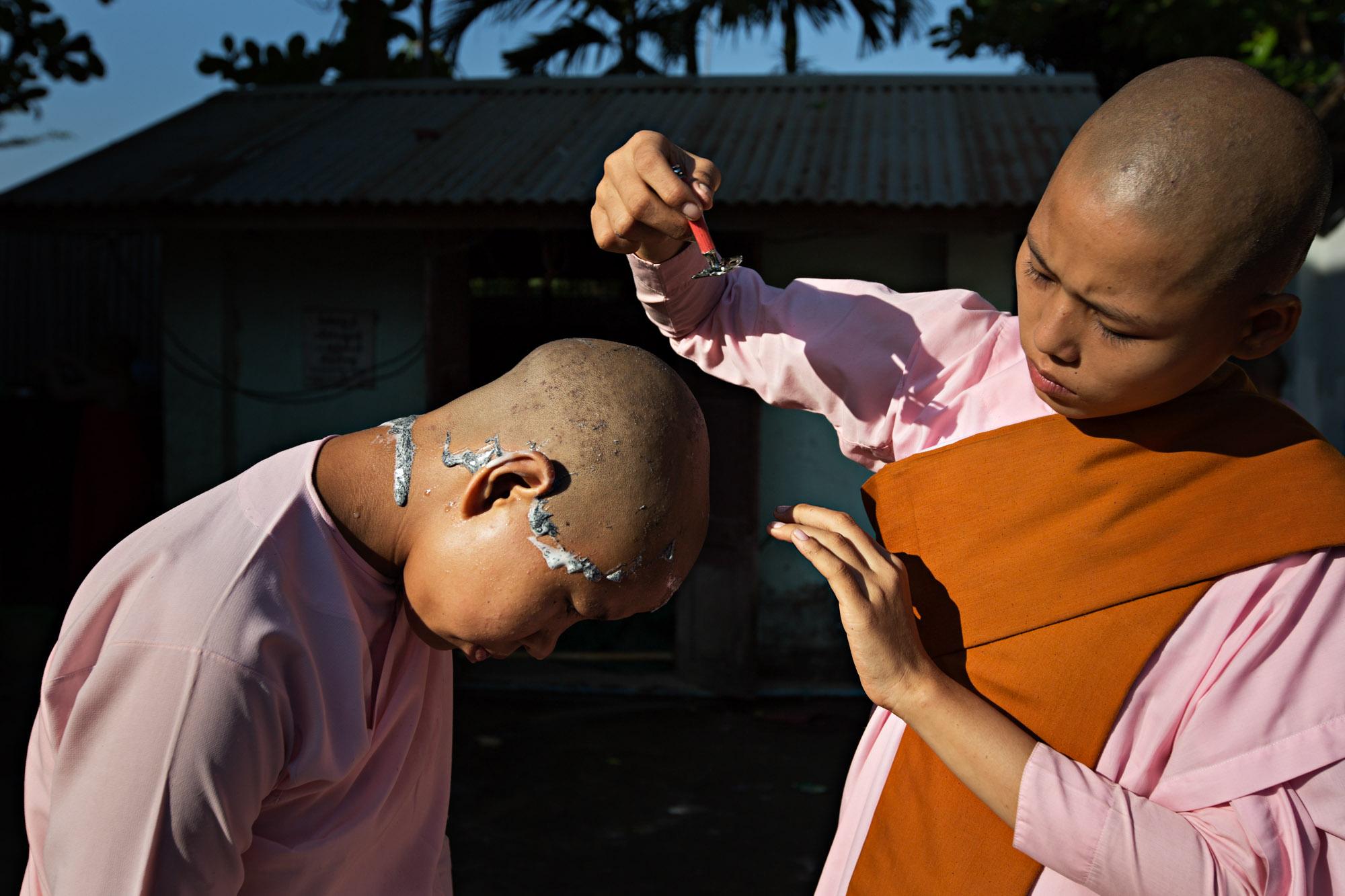 Travel - Novice Buddhist nuns assist each other in shaving their...