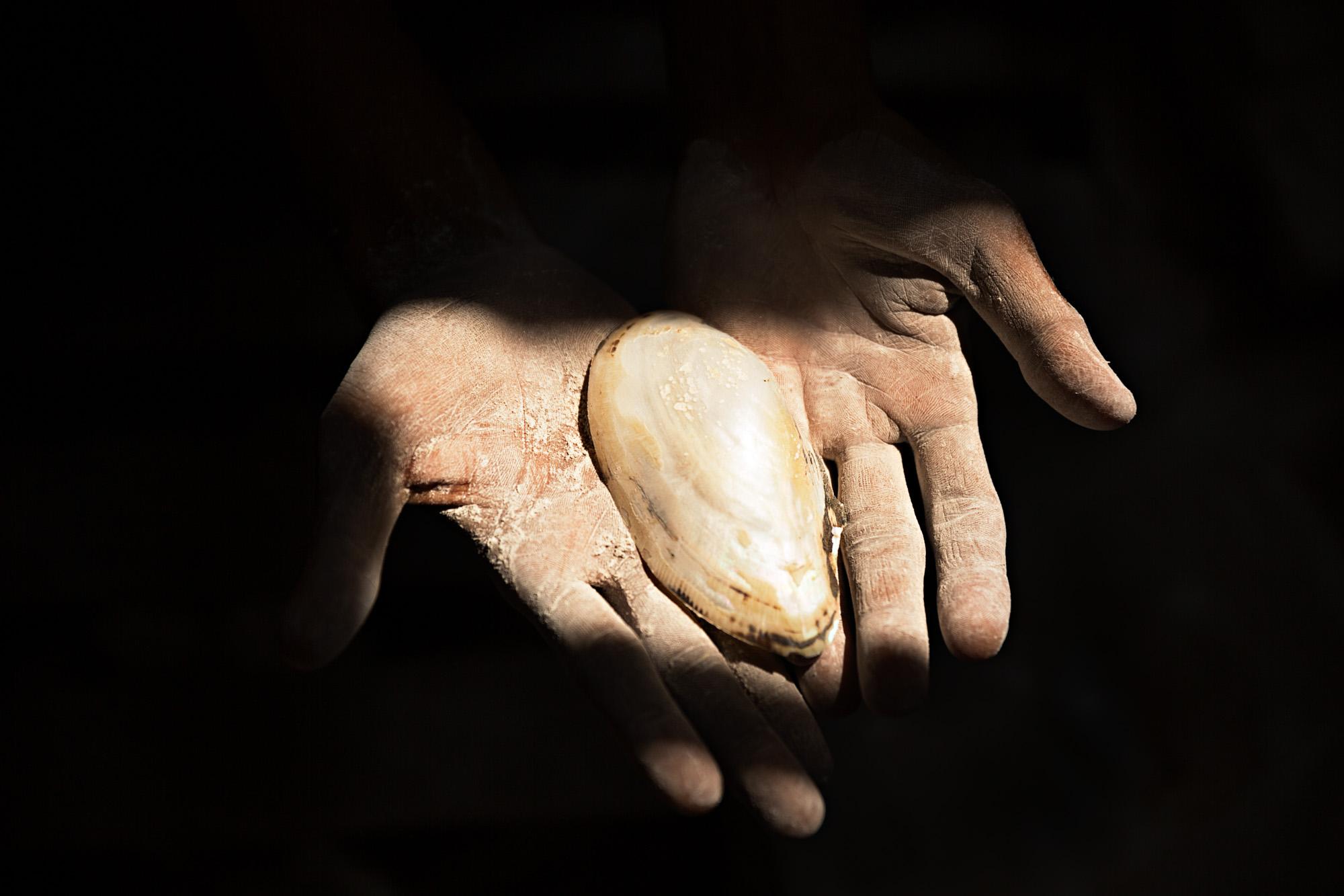 Travel - A craftsman holds a piece of shell he is using to make...