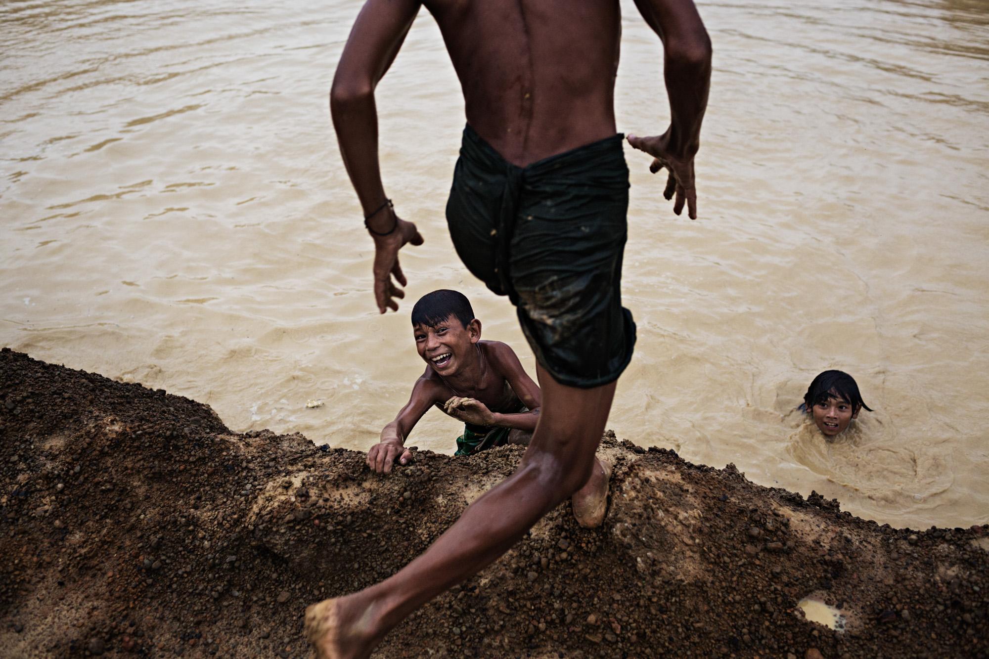 Singles -  Children swim and play in a muddy pool of water on the...