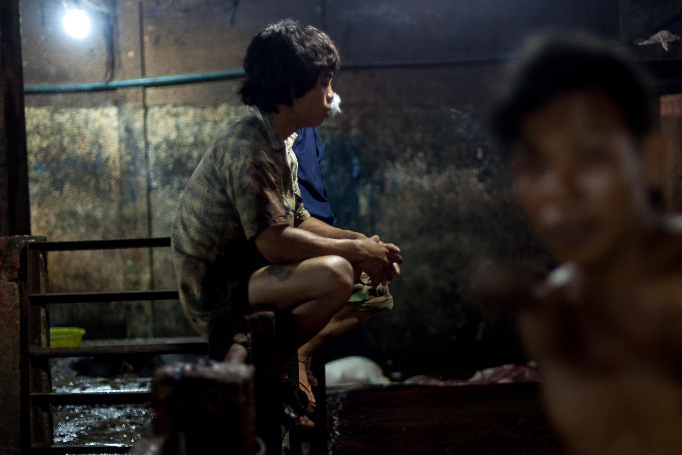 Inside a Cambodian Slaughterhouse - SIEM REAP, CAMBODIA - FEBRUARY 22: A young worker smokes...