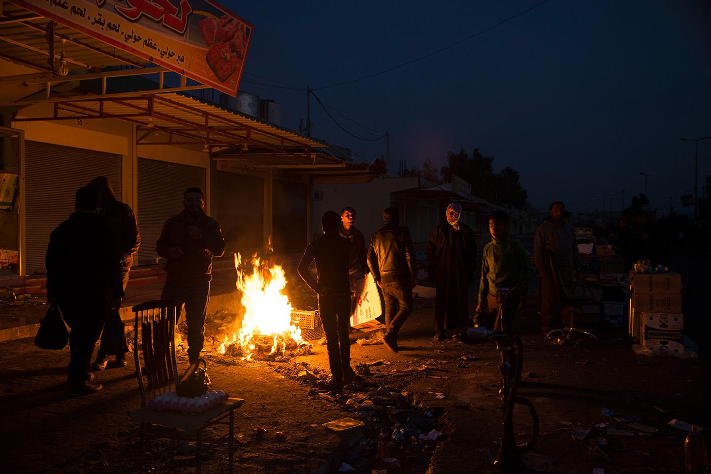 Men rest by a fire at the market in the recently liberated neighborhood of Al Sukar in eastern...