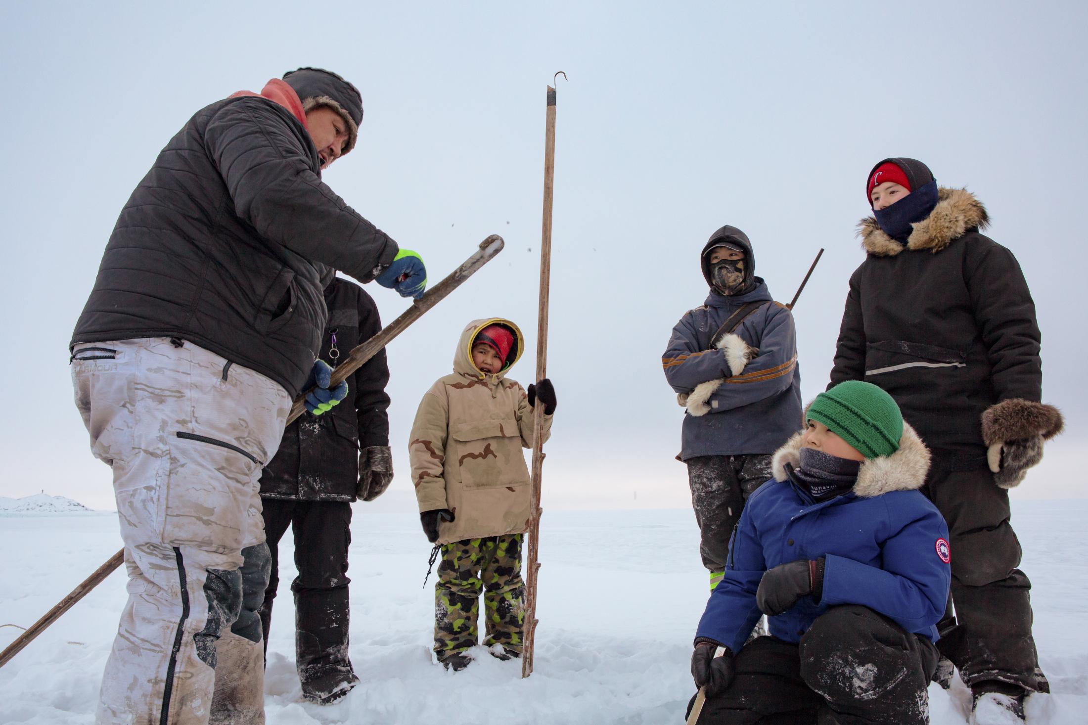 The boys watch as Kevin Kullualik demonstrates how to scrape off ice from a seal hook (niksik),...