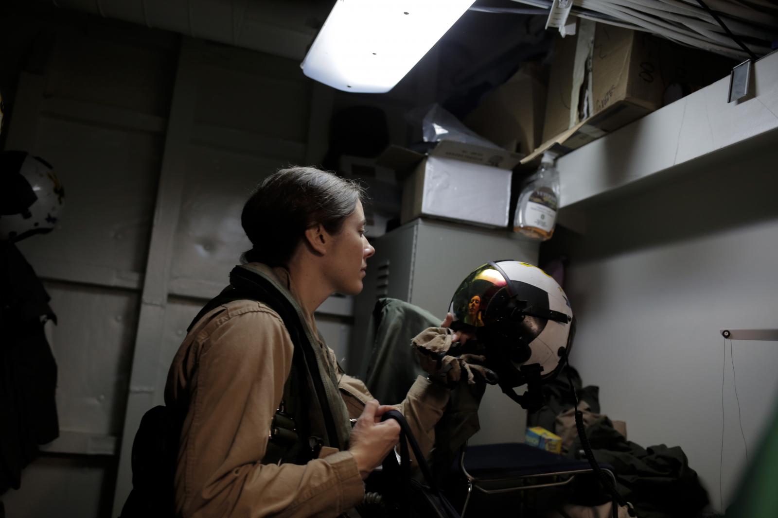 A pilot of one of the fighter jets onboard the USS George H.W. Bush aircraft carrier, looks at herself in the reflection of her helmet as she prepares for a take off.
