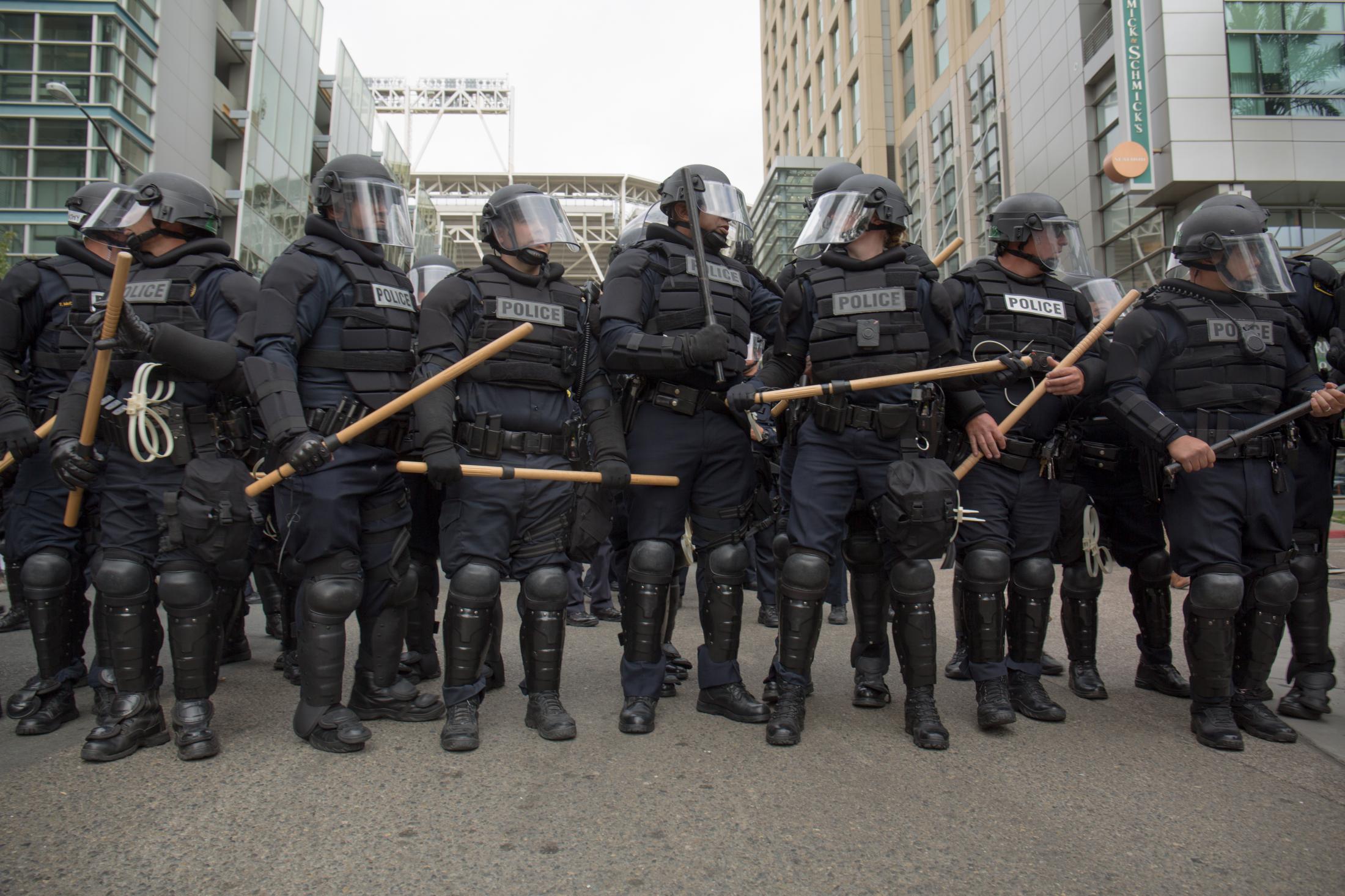 News - Police in riot gear hold batons outside of the San Diego...