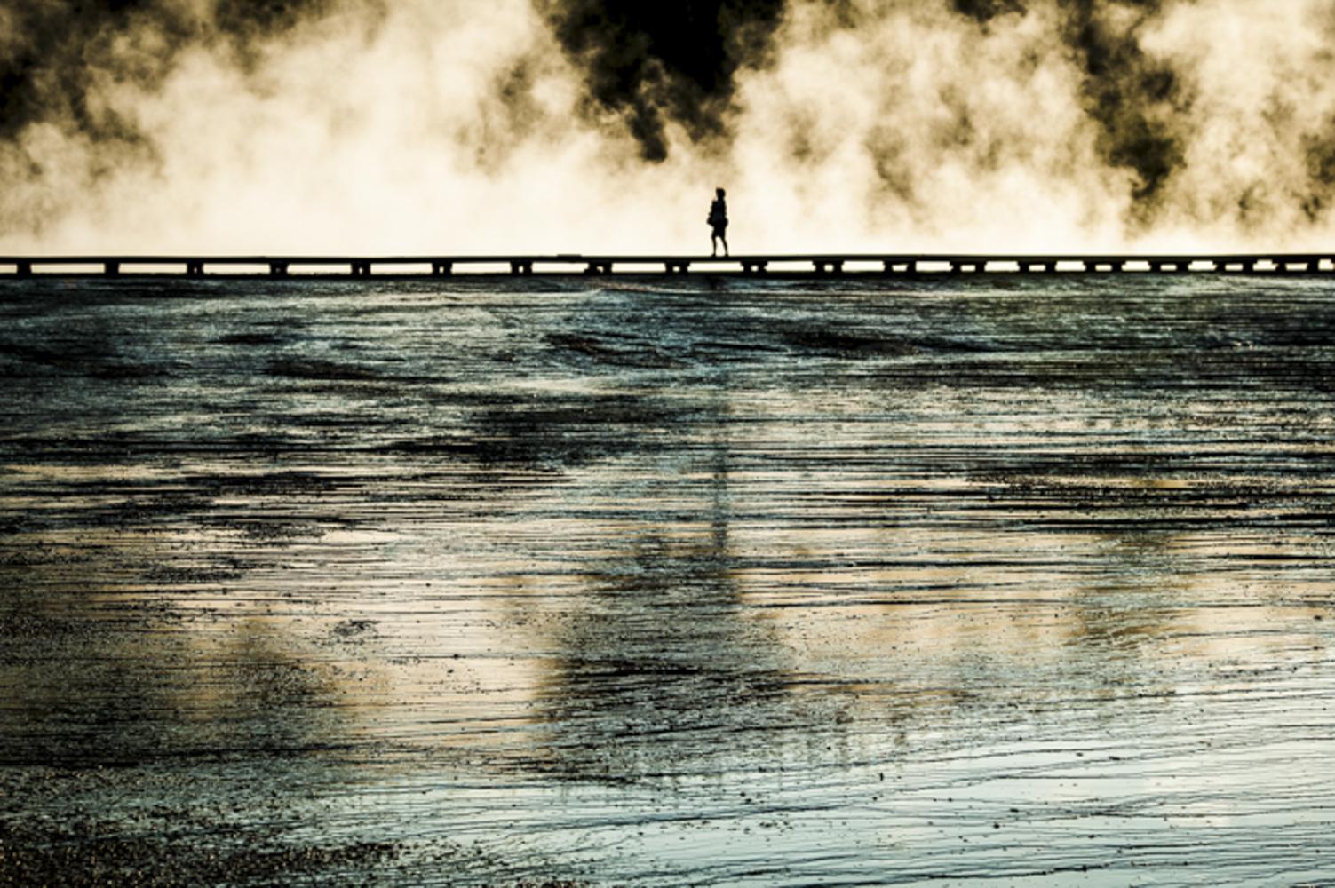 A women walks on a plank overlooking a geyser in Yellowstone National Park, California.