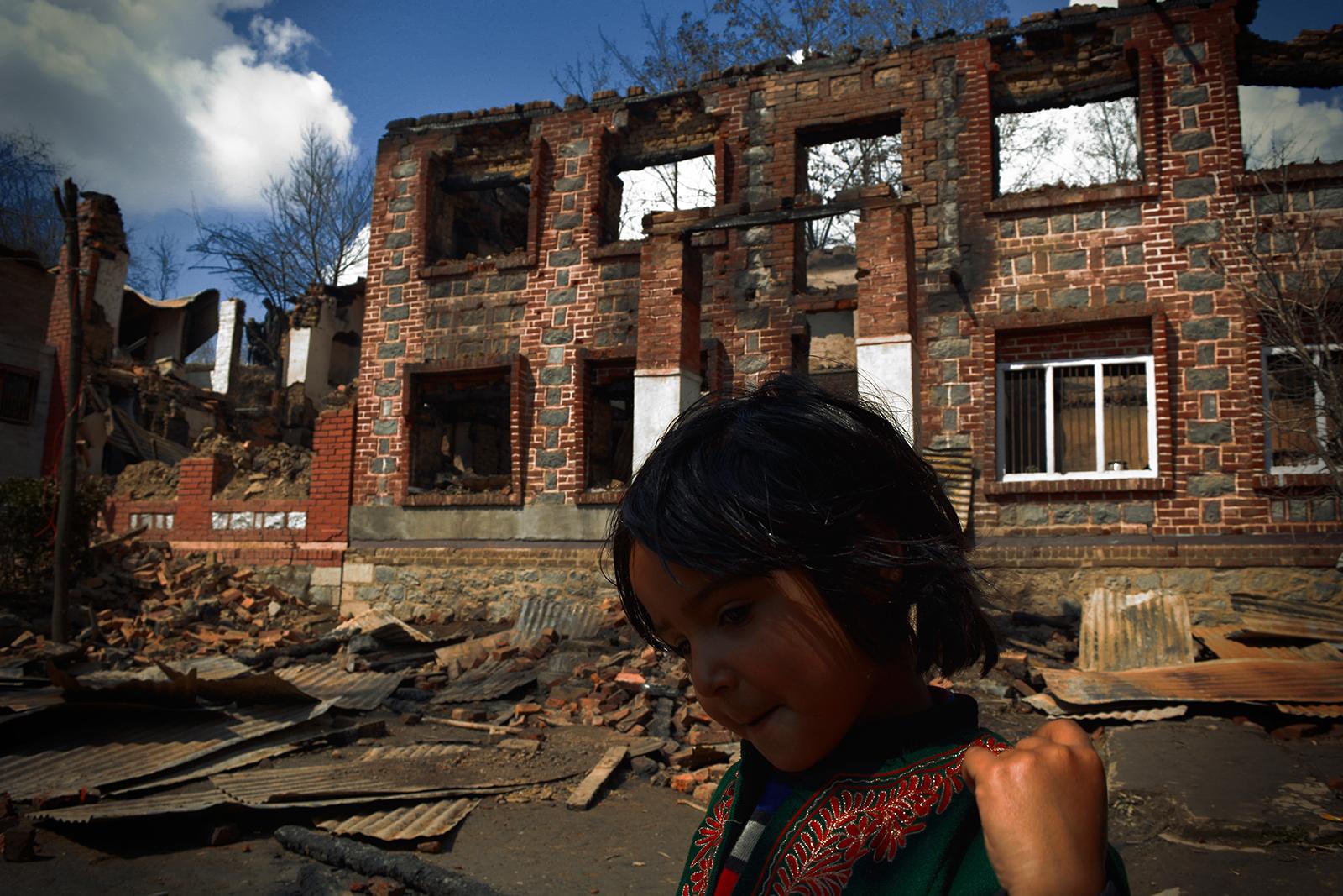 Kashmir-The Never Ending War - A girl walks past the ruins of a bombed house of a poet...