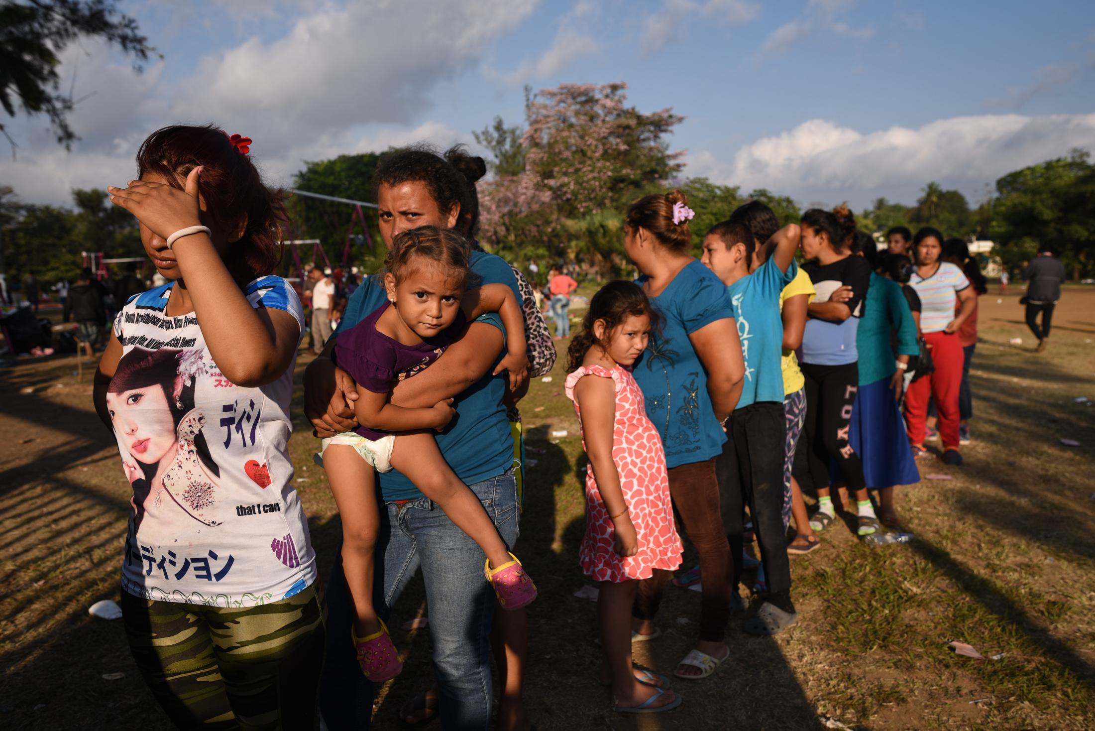 Mujeres y ni&ntilde;os migrantes se forman para recibir alimentos en un centro deportivo de...