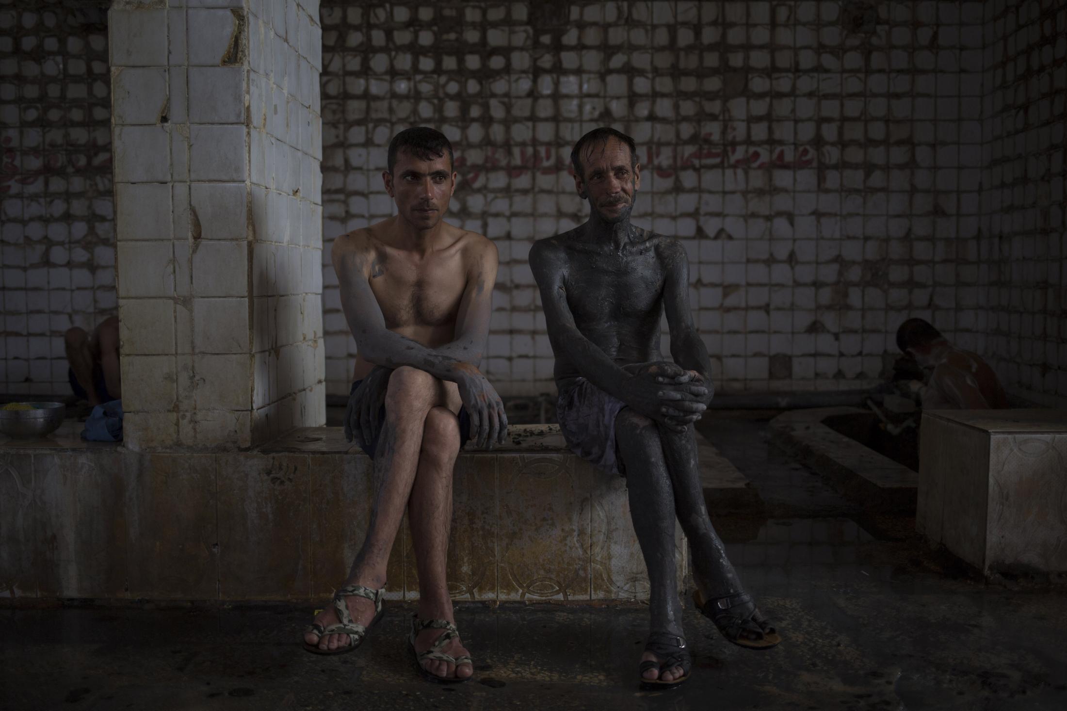 Two customers of the Hamam Alil spa south of Mosul, Iraq, take a break from bathing after covering themselves with mud from a nearby sulphur well,...