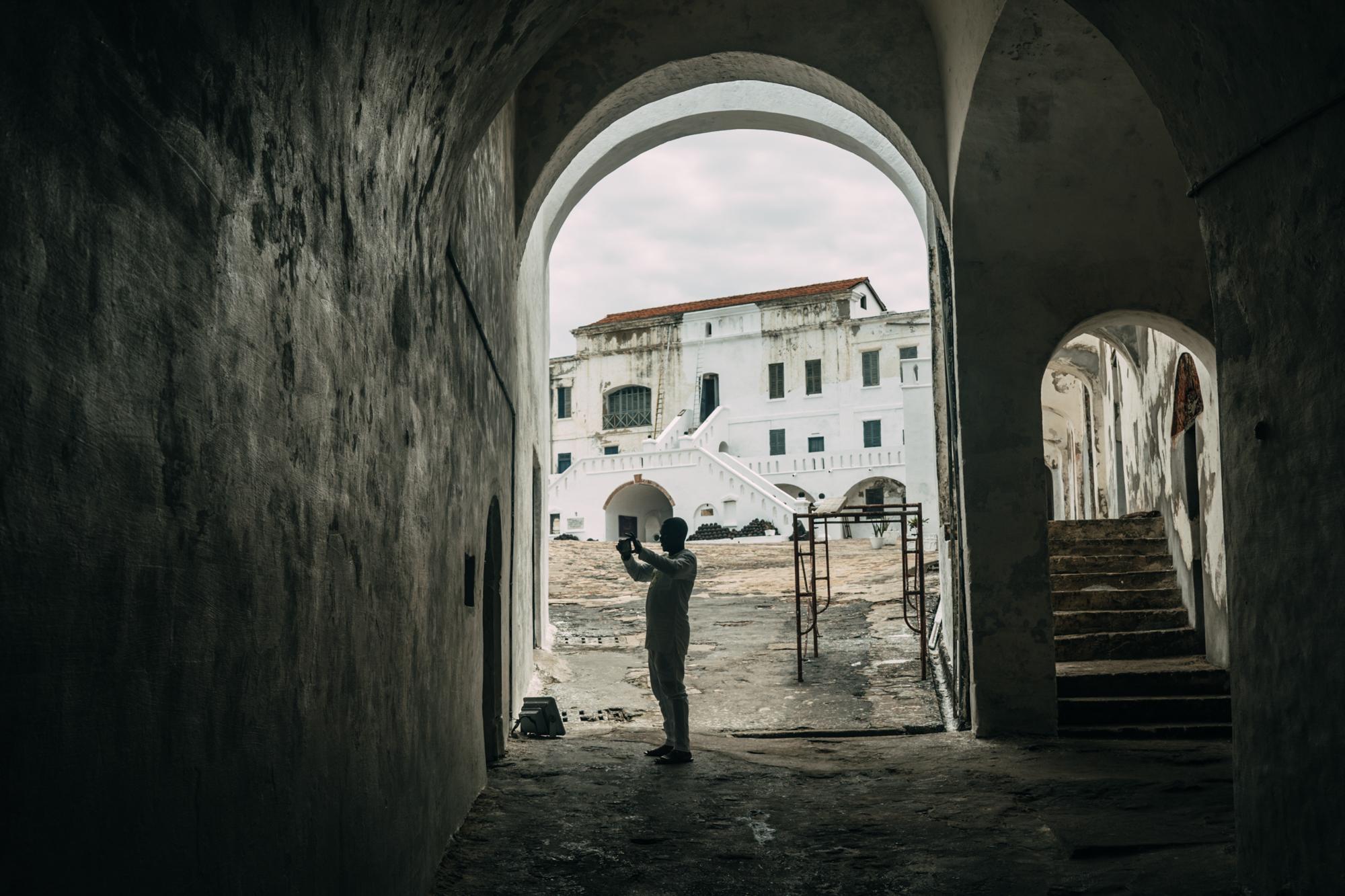 The Year of Return - A man takes a picture of a dungeon at the Cape Coast Castle.