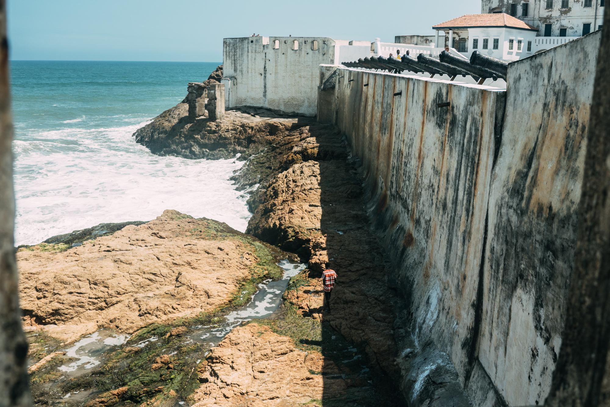 The Year of Return - A man walks on the rocks outside of the Cape Coast Castle.