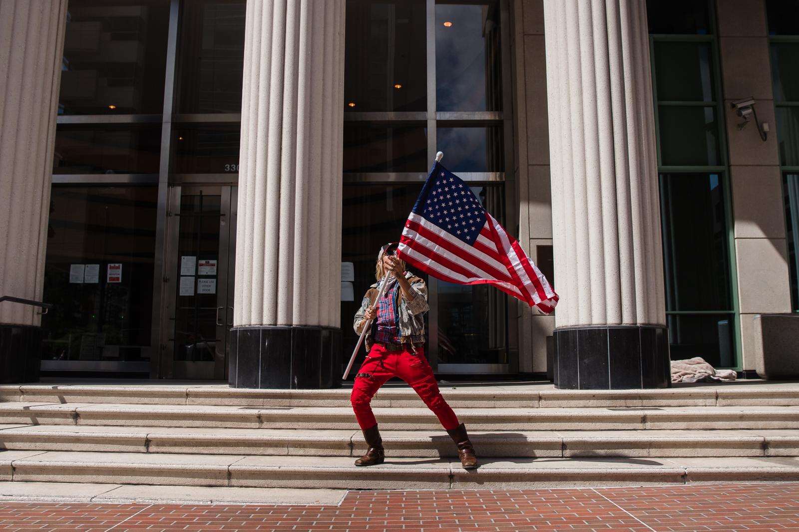 A man waves the American flag in front of the Hall of Justice Courthouse while protesters rally in downtown San Diego against California&#39;s stay at home order to prevent the spread of Coronavirus on April 18, 2020. With growing frustration there have been other planned demonstrations in several cities across the United States.