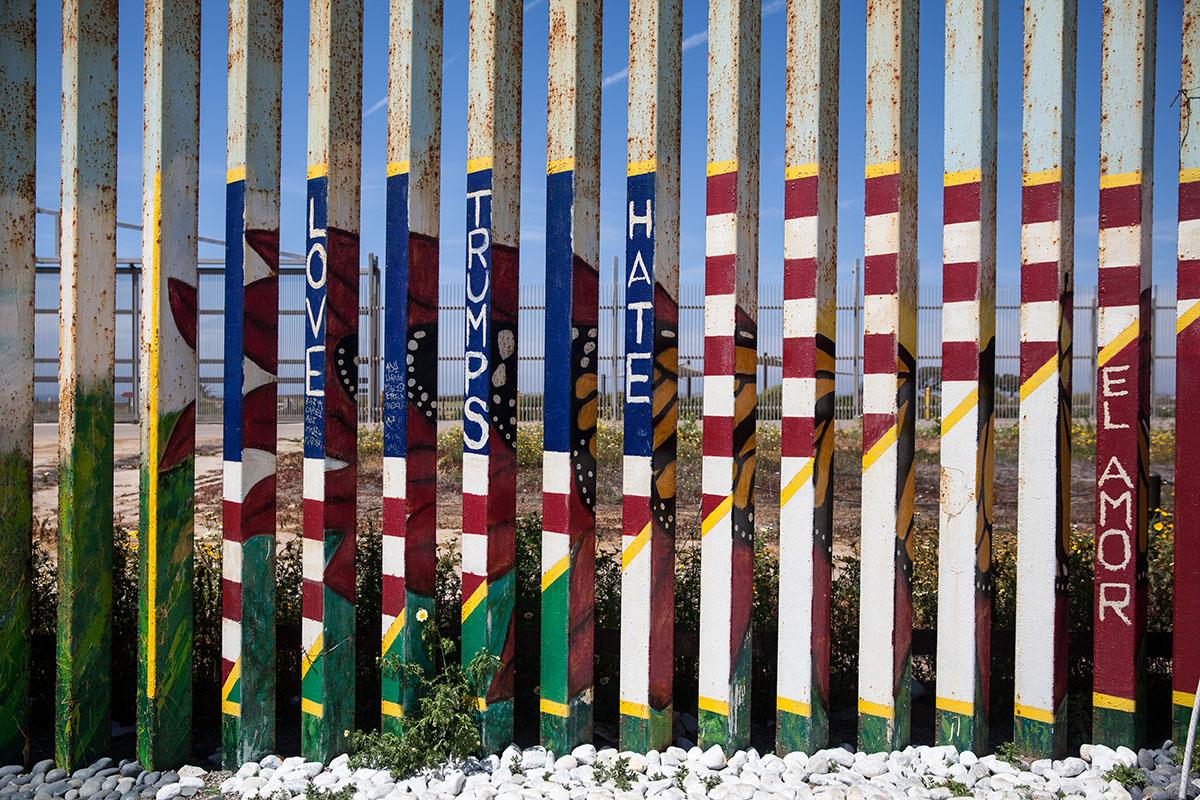 The border fence from the Mexican side is painted with vibrant colors often reflecting the...