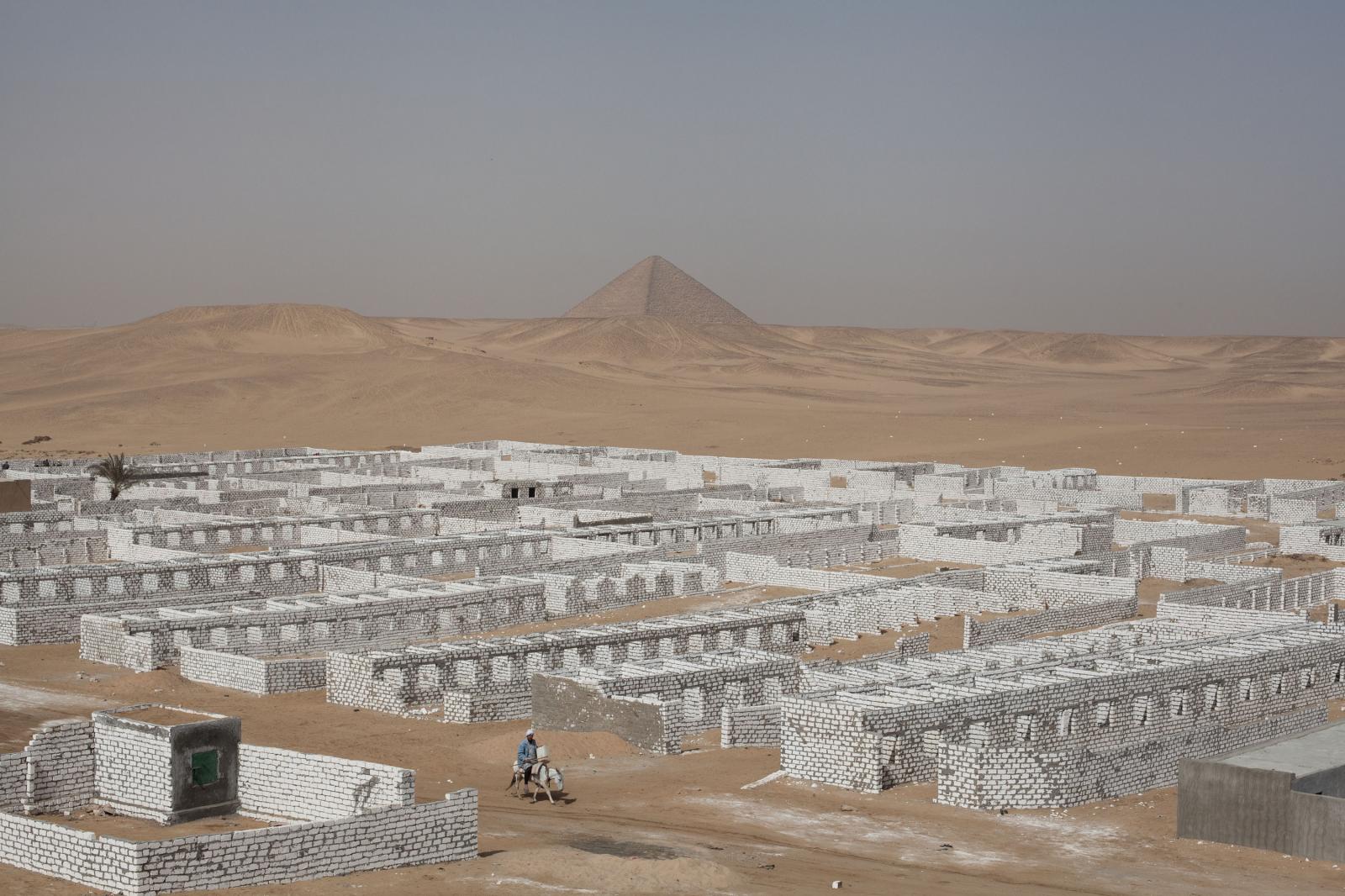 A man on a donkey passing through a white stone wall cemetery. &nbsp;Sneferu&#39;s first smooth sided Red Pyramid can be seen in the distance.