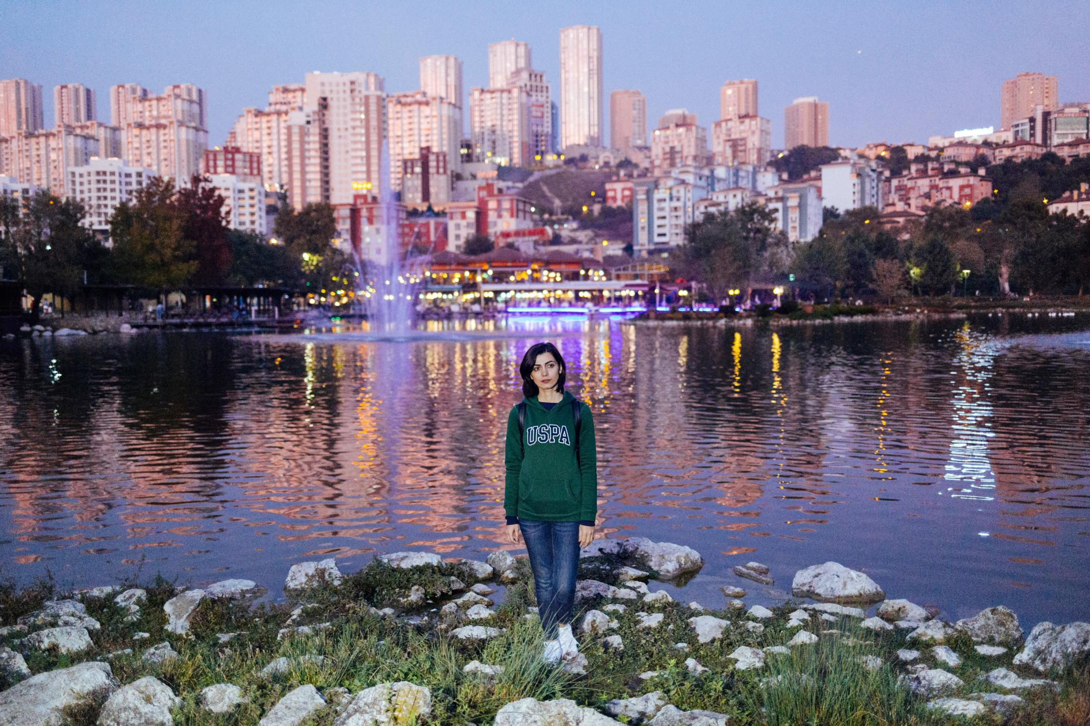 The Pursuit of Happiness -  Helen (30), stands by the water in front of a cityscape....