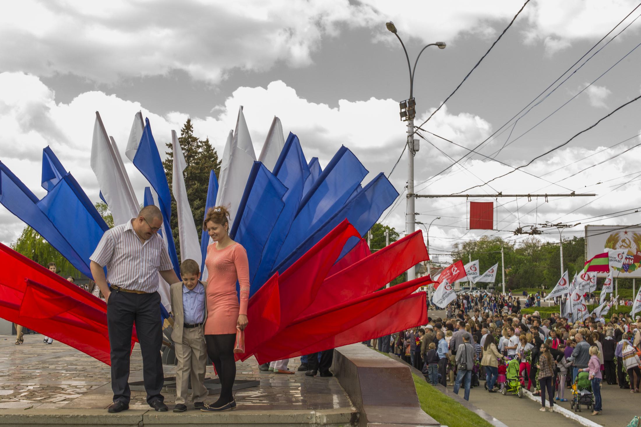  A family stands for a picture in front of a decoration made of flags with the Russian...
