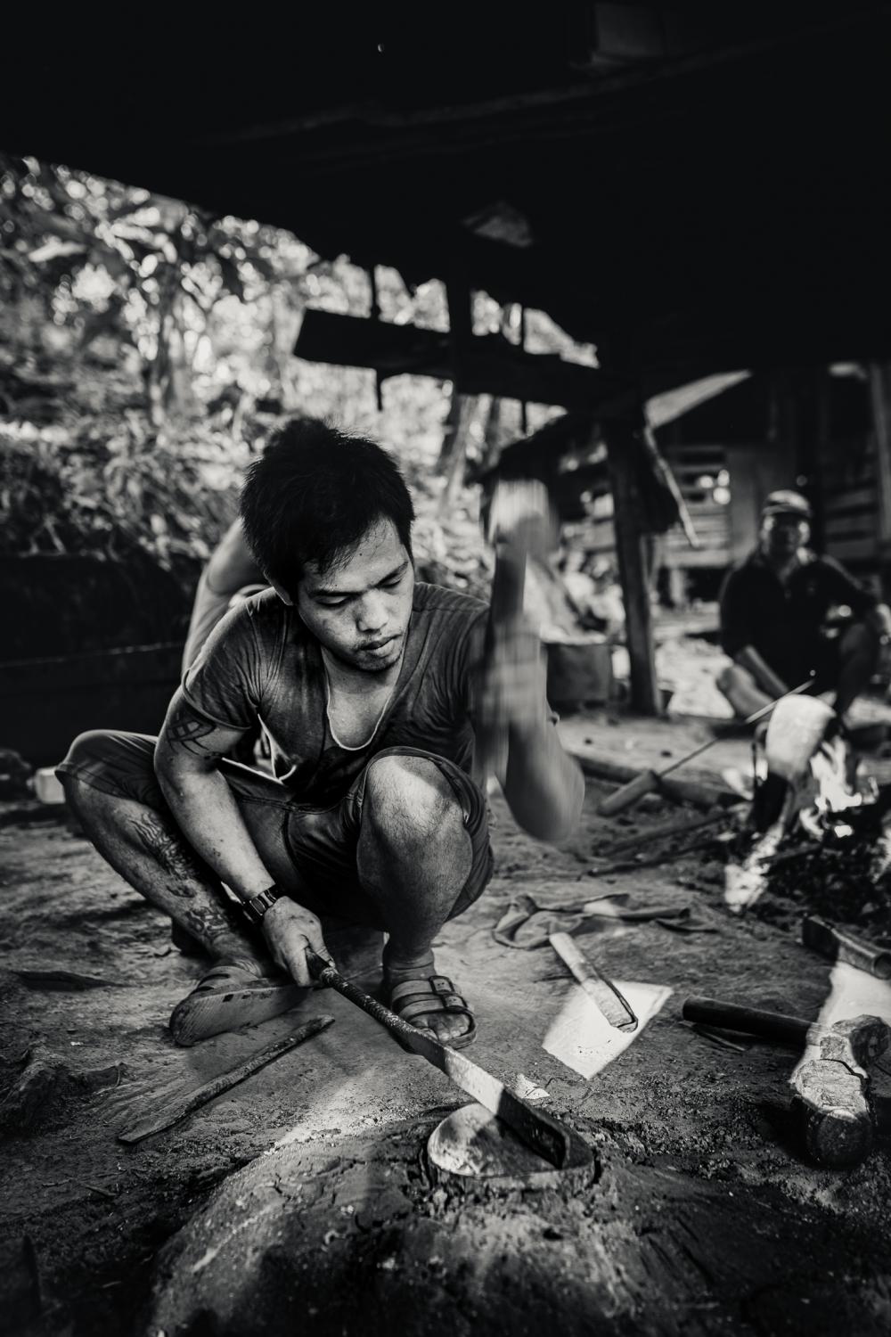 Indigenous Land Rights in Sarawak -  A metal worker hammers out a parang blade in the Long...