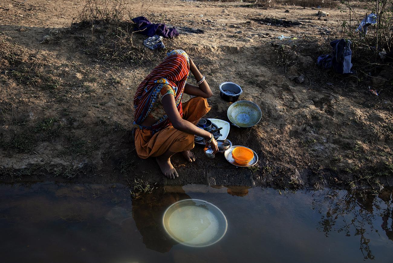 Migrant workers in Bhopal - Migrant women washing dishes in a polluted water near...