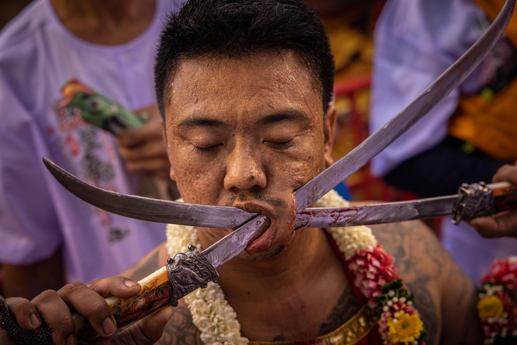 Singles - A devotee has his cheek pierced with two swords as a way...