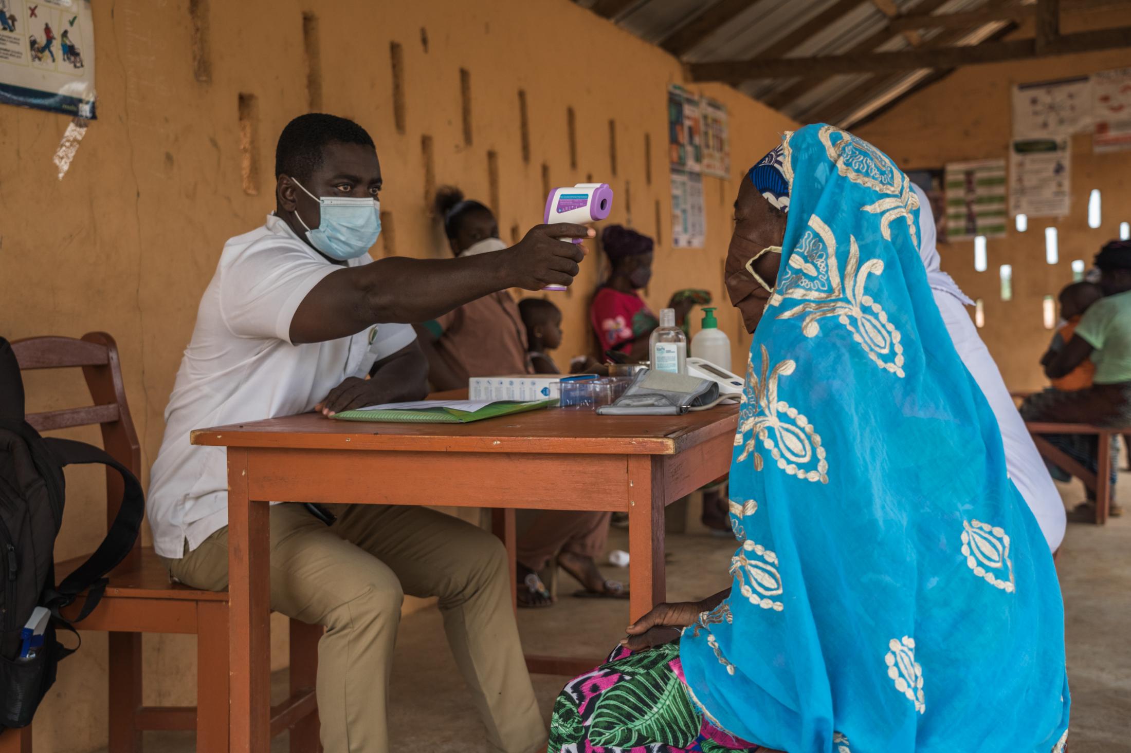 Covid-19 Response in Northern Ghana - Tinguri Clinic health worker checks the temperature of...