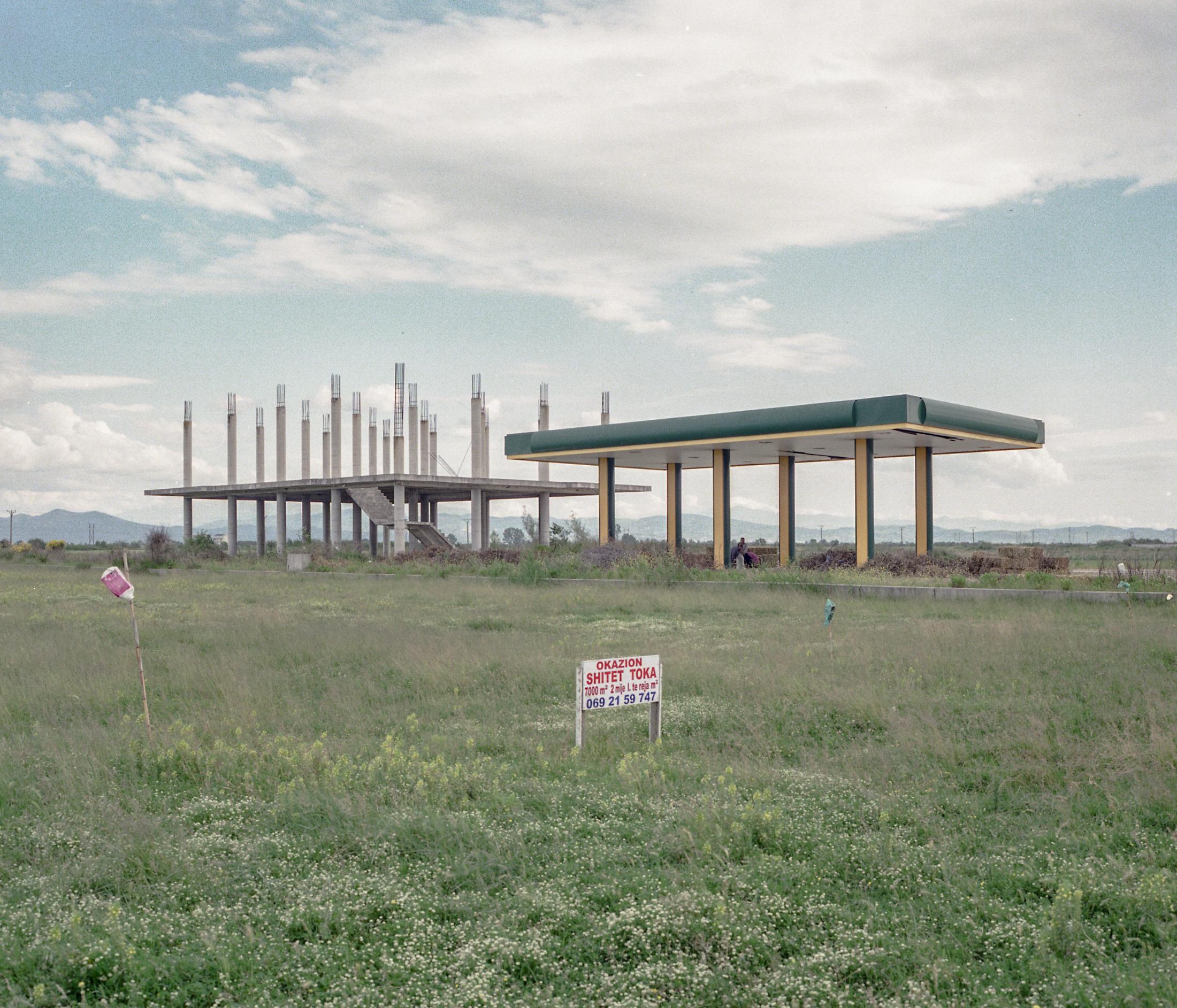 Dismantled buildings, abandoned gas stations and plots for sale are a common part of the Albanian landscape. In the photograph, a dismantled structure next to a service station that has been converted into a hay warehouse for the surrounding farmers in Lushnj&euml;. May 2019.