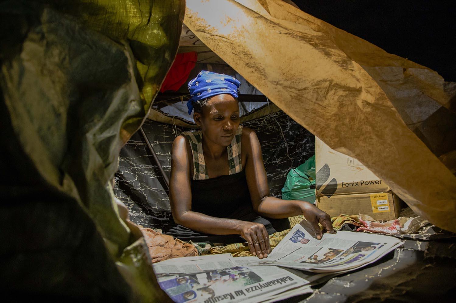 Gertrude (45), a Nakawa Market vendor, reads a newspaper in a self-made tent where she spends her...
