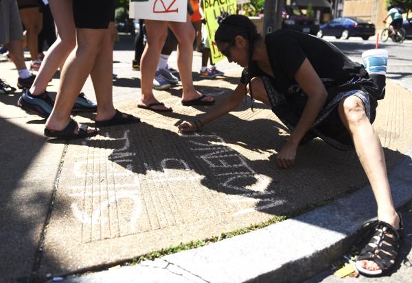 A woman marks the sidewalk with chalk that reads &#39;silence is violence,&#39; at a protest on Sunday, June 7, 2020, on Tucker Blvd. in St. Louis. Demonstrators from many races and backgrounds march in solidarity at protests across the nation.