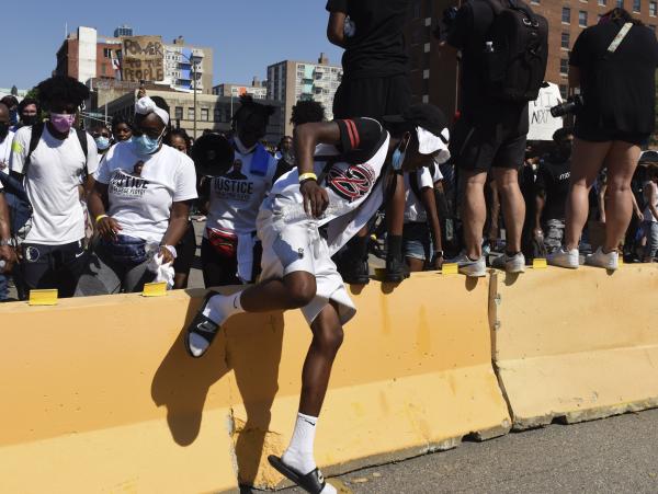 Image from Black Lives Matter: A Nation In Protest - A protestor jumps over the concrete baracade blocking...