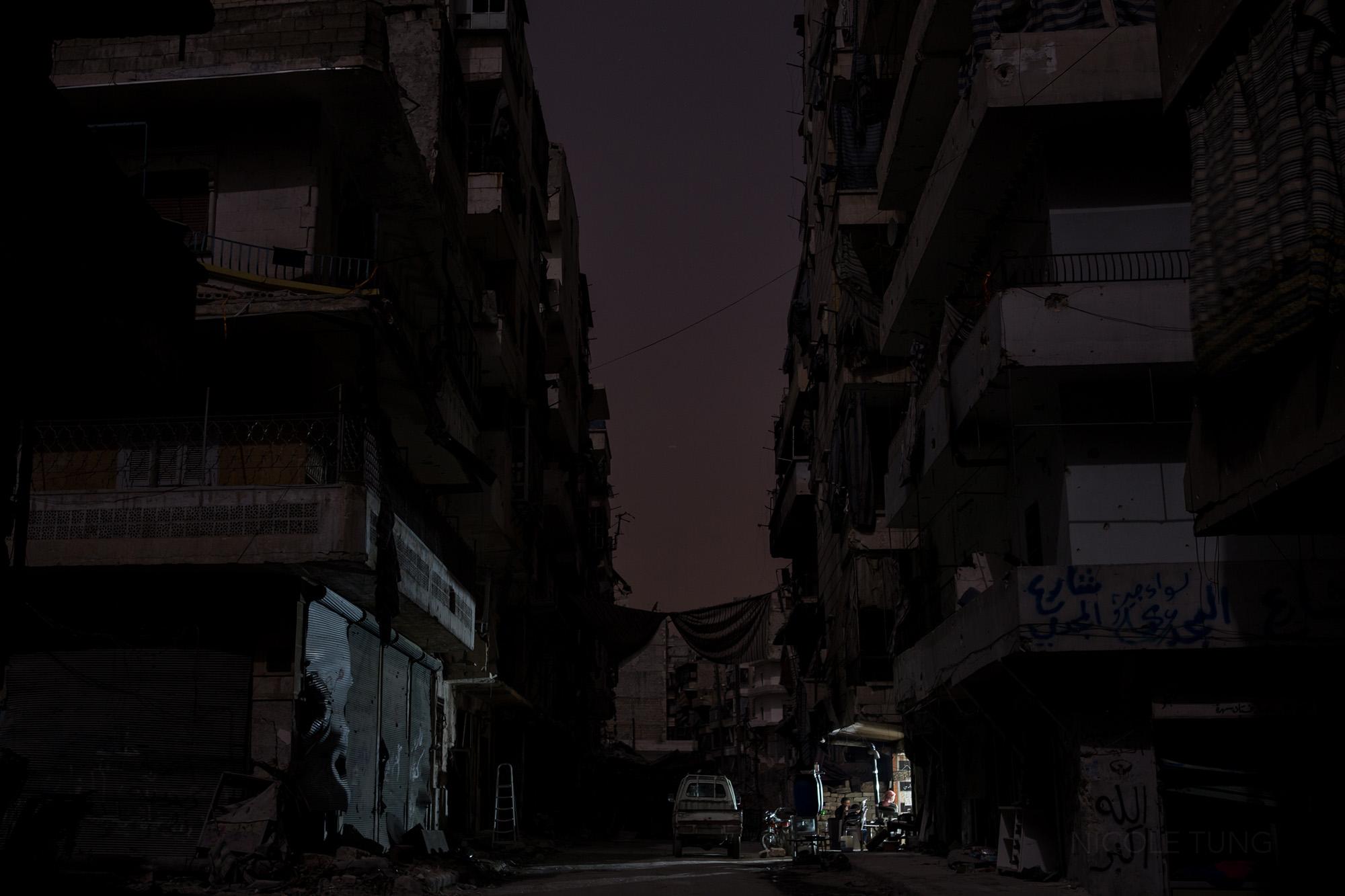 Syria: The Long Night - Damaged buildings and curtains over a street in Aleppo,...