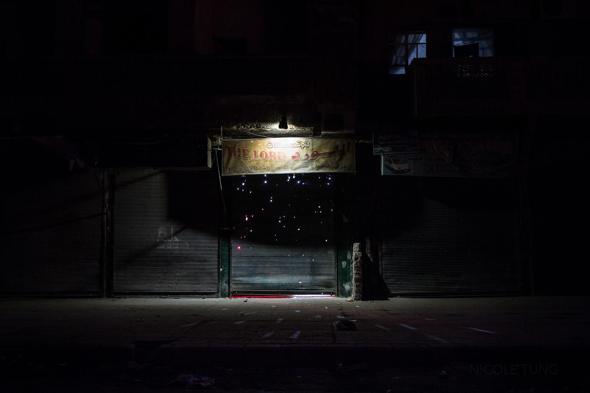 Rays of light shine through a shrapnel ridden metal gate enclosing a store, Aleppo, Syria. March 2013.&nbsp;