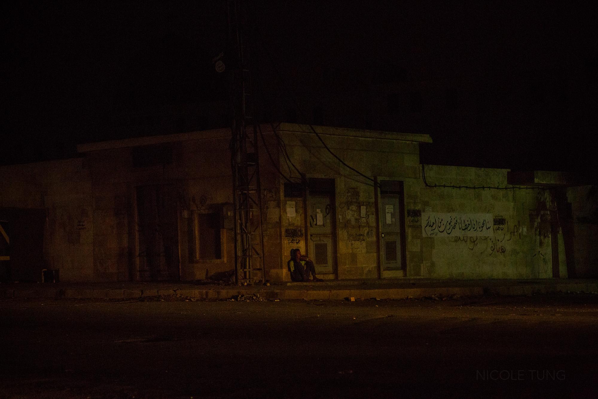 A man sits at the corner of two streets in a rebel held neighborhood of Aleppo, Syria. May 2013.&nbsp;
