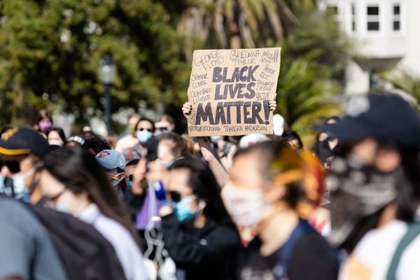Image from Protests -  A protester holds a sign at Mission Dolores Park in a...