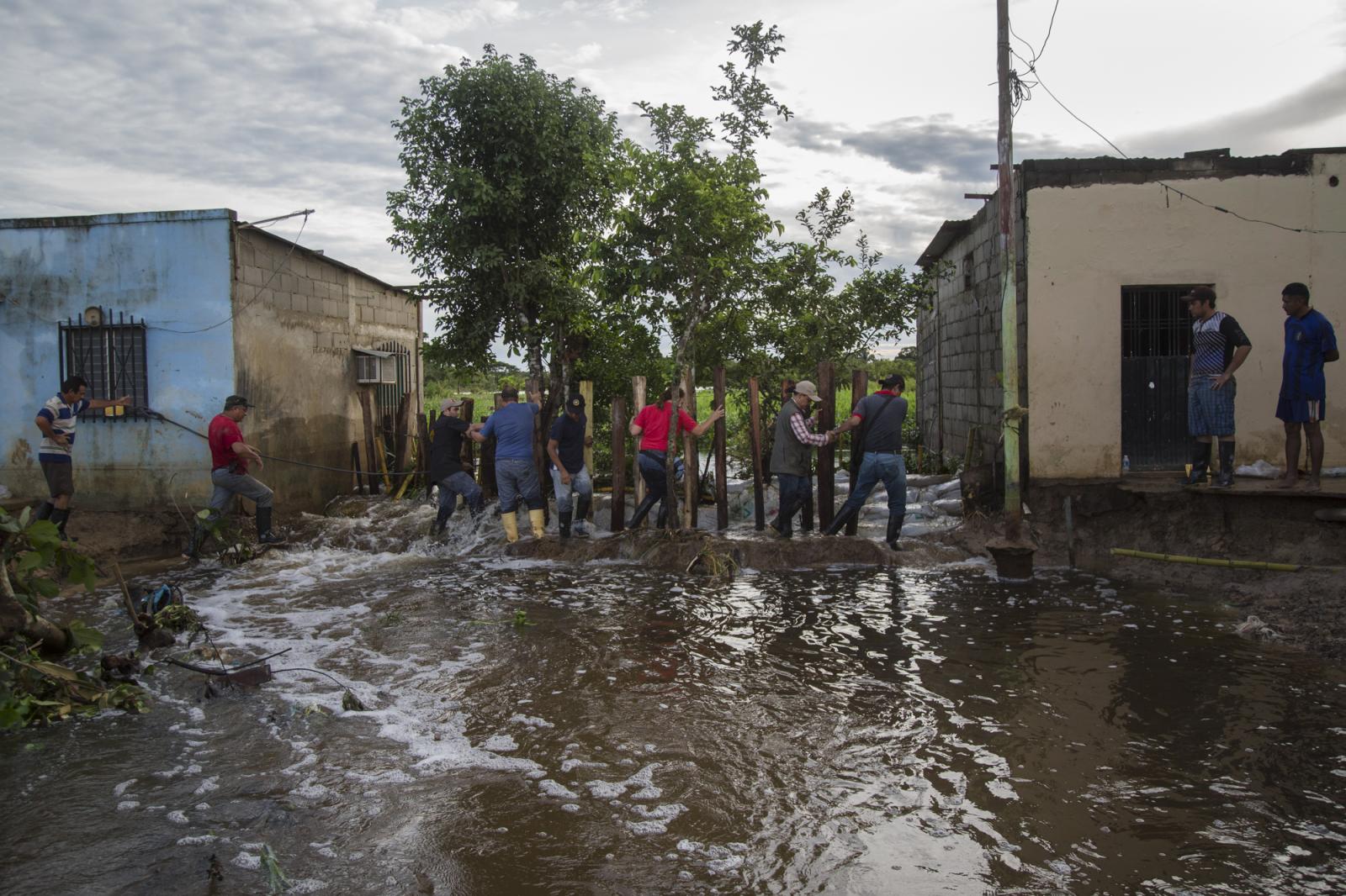  Un grupo de personas cruza el r&iacute;o desbordado, mientras una cuadrilla de trabajadores intenta frenar el agua, en Guasdualito, el 6 de julio de 2015. 
