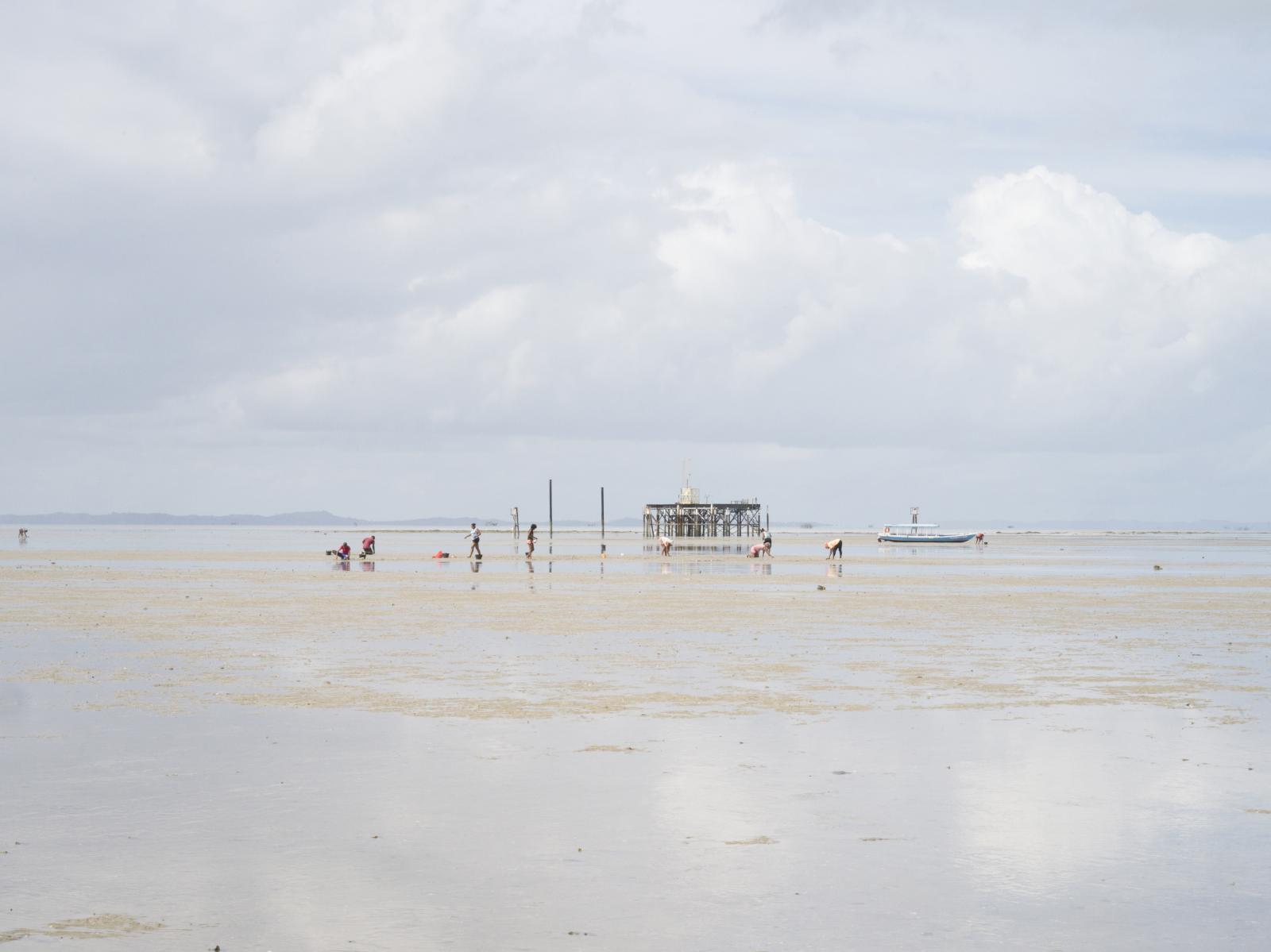 Ilha da Mar&eacute;, Bahia. Shell collectors search for clams in front of an extration oil...