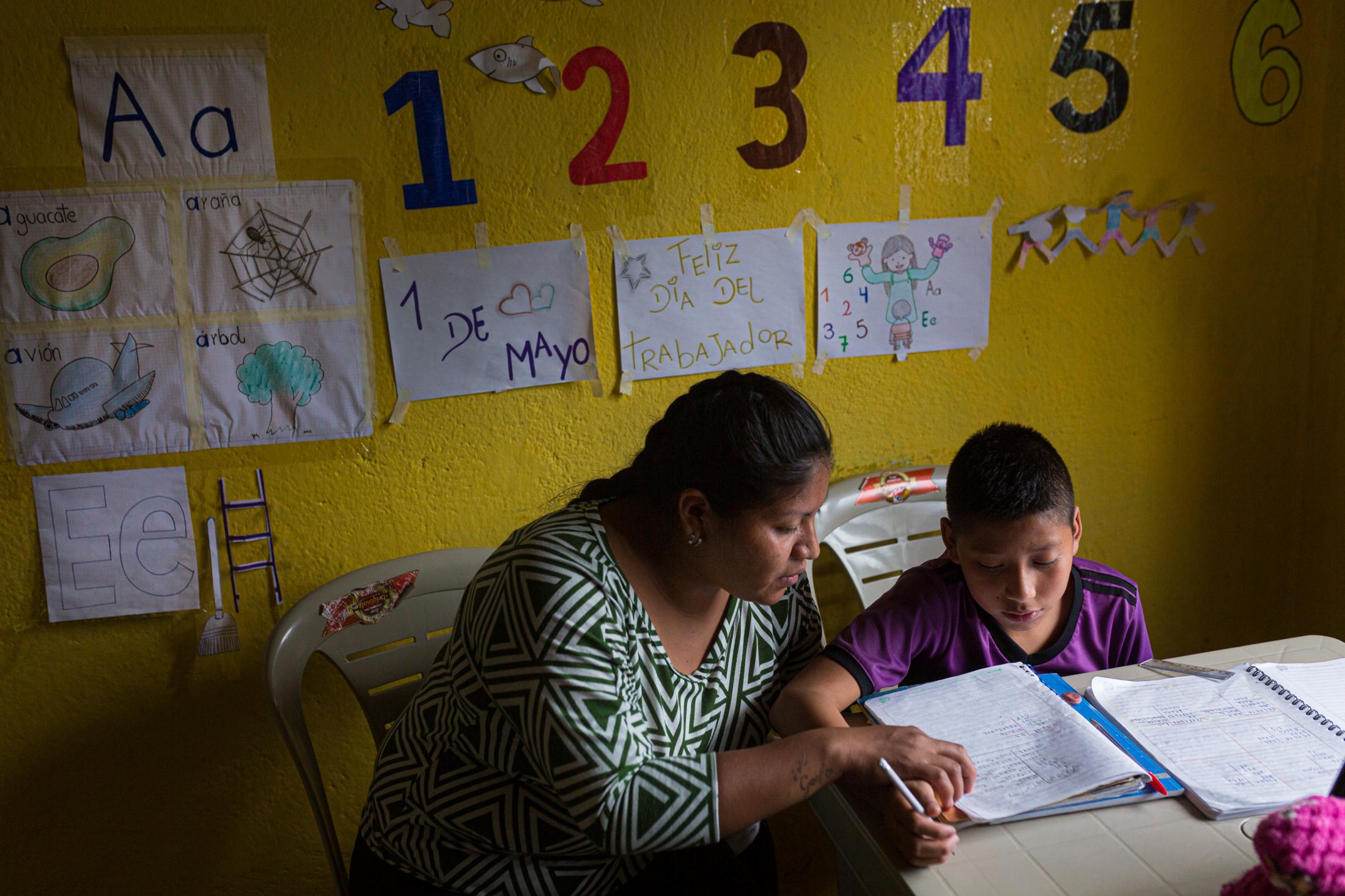 Erika Pozo helps her nephew Josthyn Neira (12), a seventh grade student at Ruperto Alarc&oacute;n Falcon&iacute; School, to do some math operations that are part of the homework that his teacher sends him through whatsapp daily. Josthyn lives together with her aunt&#39;s family in the central part of the parish of Cotogchoa where there is the possibility of hiring internet home service. However, they don&#39;t have money to have that service, but a neighbor shares her wifi network so Jhostyn and one of his cousins can access their homework. May 29, 2020. Cotogchoa-Ecuador. Andr&eacute;s Y&eacute;pez.