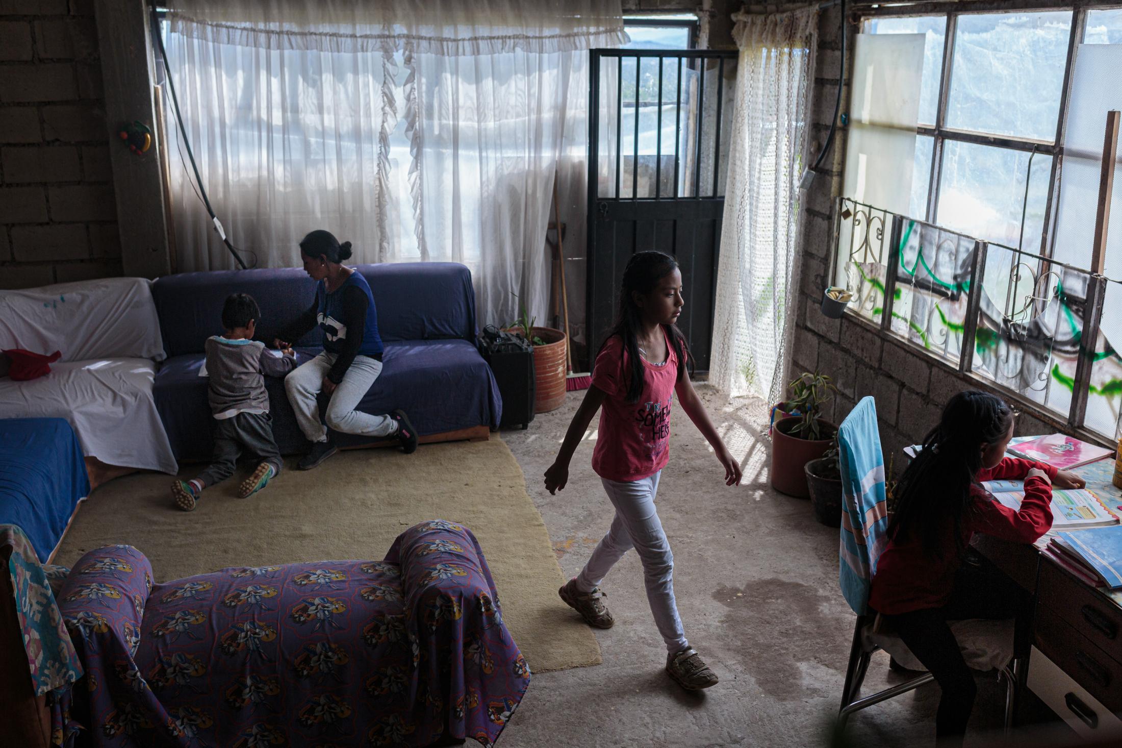 Maribel Loacham&iacute;n (32) helps her son Angelo Andrade (7) with his homework in the living room, while her older daughter Sof&iacute;a Andrade (11) helps her other daughter Sarah&iacute; (9) at her desk. They don&#39;t have a phone so they can receive homework through Whatsapp. The teacher comes once a week to drop off printed homework guides for the entire week. June 22, 2020. Cotogchoa-Ecuador. Andr&eacute;s Y&eacute;pez