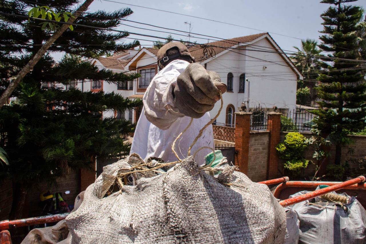 Katumba Badru | My Trash, Your Trash - A worker sits atop a vehicle as it carries waste from the...