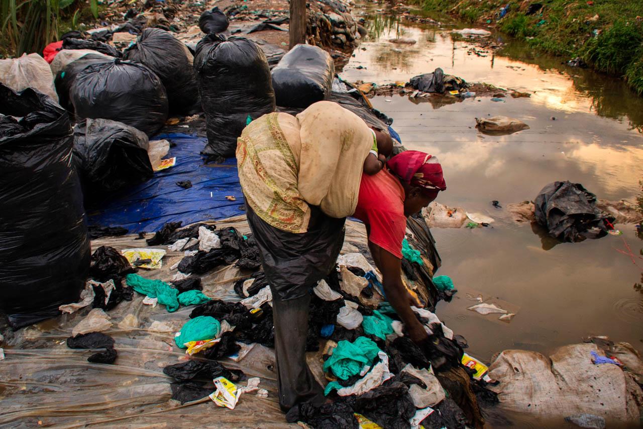 A woman carries her baby as she cleans plastic bags which will then be sold to a factory that recycles them into home plastic utensils such as basins, plates and cups.