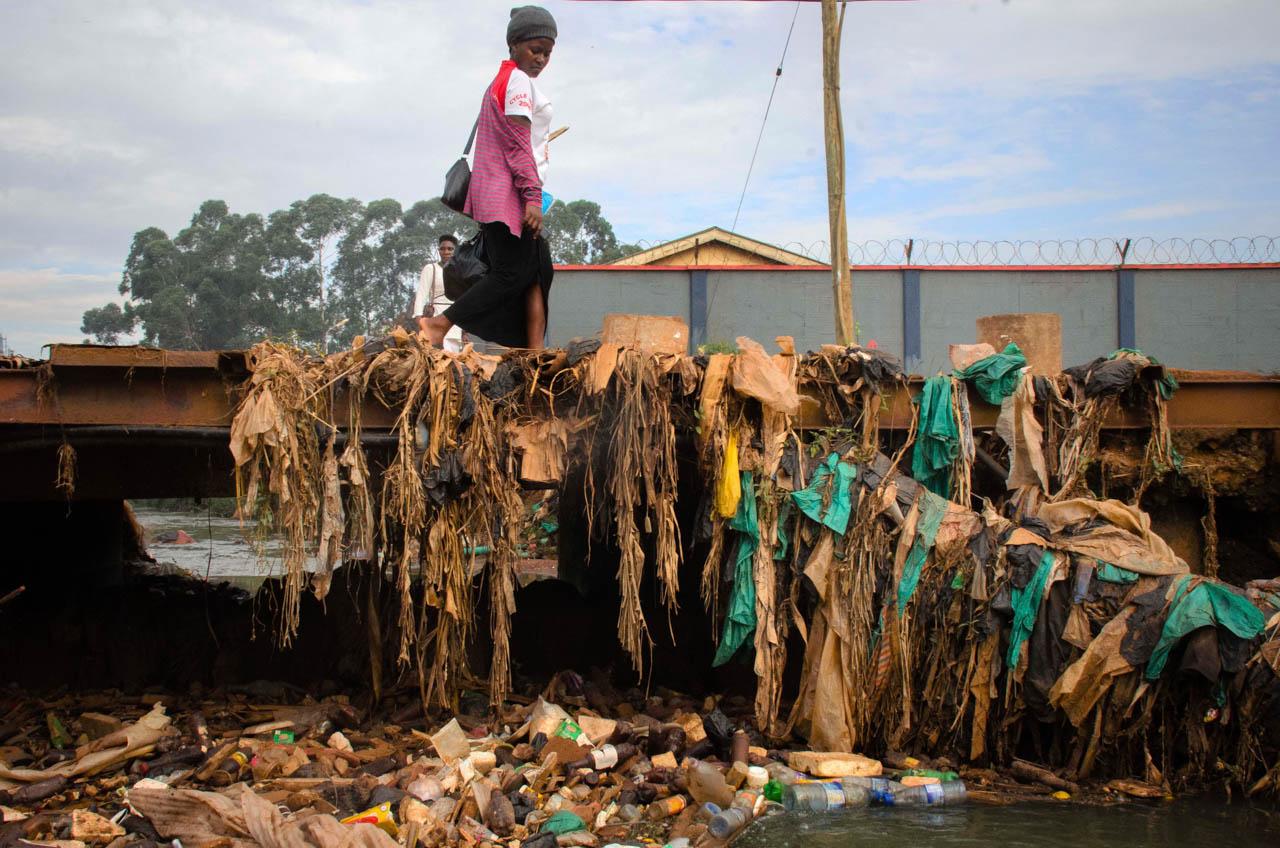 Katumba Badru | My Trash, Your Trash - A woman walks over a bridge covered with plastic bags and...