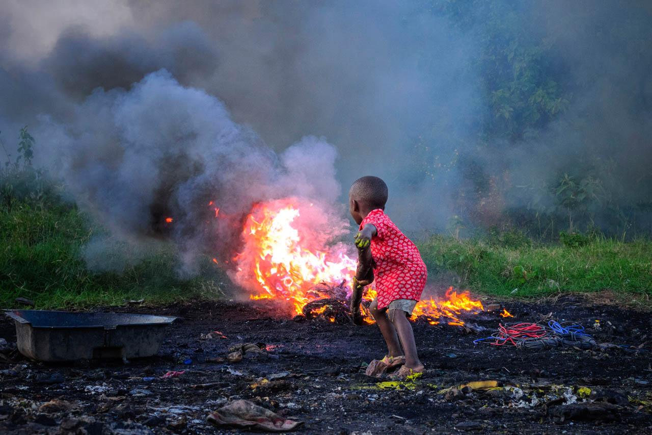 A little boy burns plastic bags in front of his home in Gayaza, Uganda.