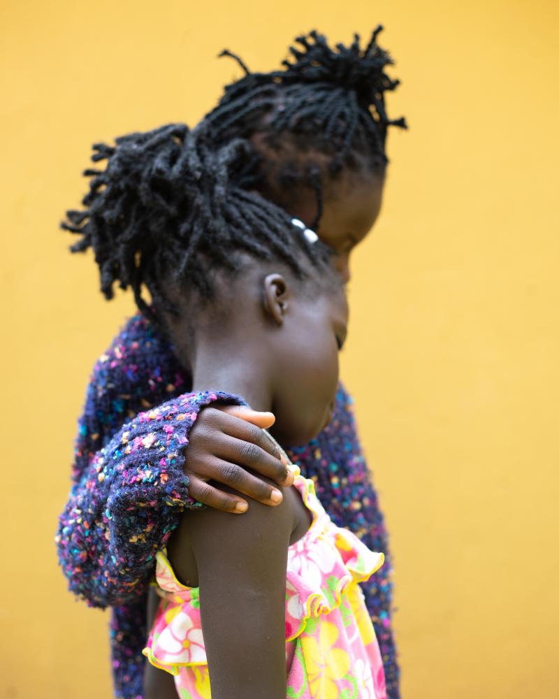 Image from Surviving Bery: A Girlhood Trauma | DeLovie Kwagala  - Blessing*, 8 years old, comforts the youngest survivor,...