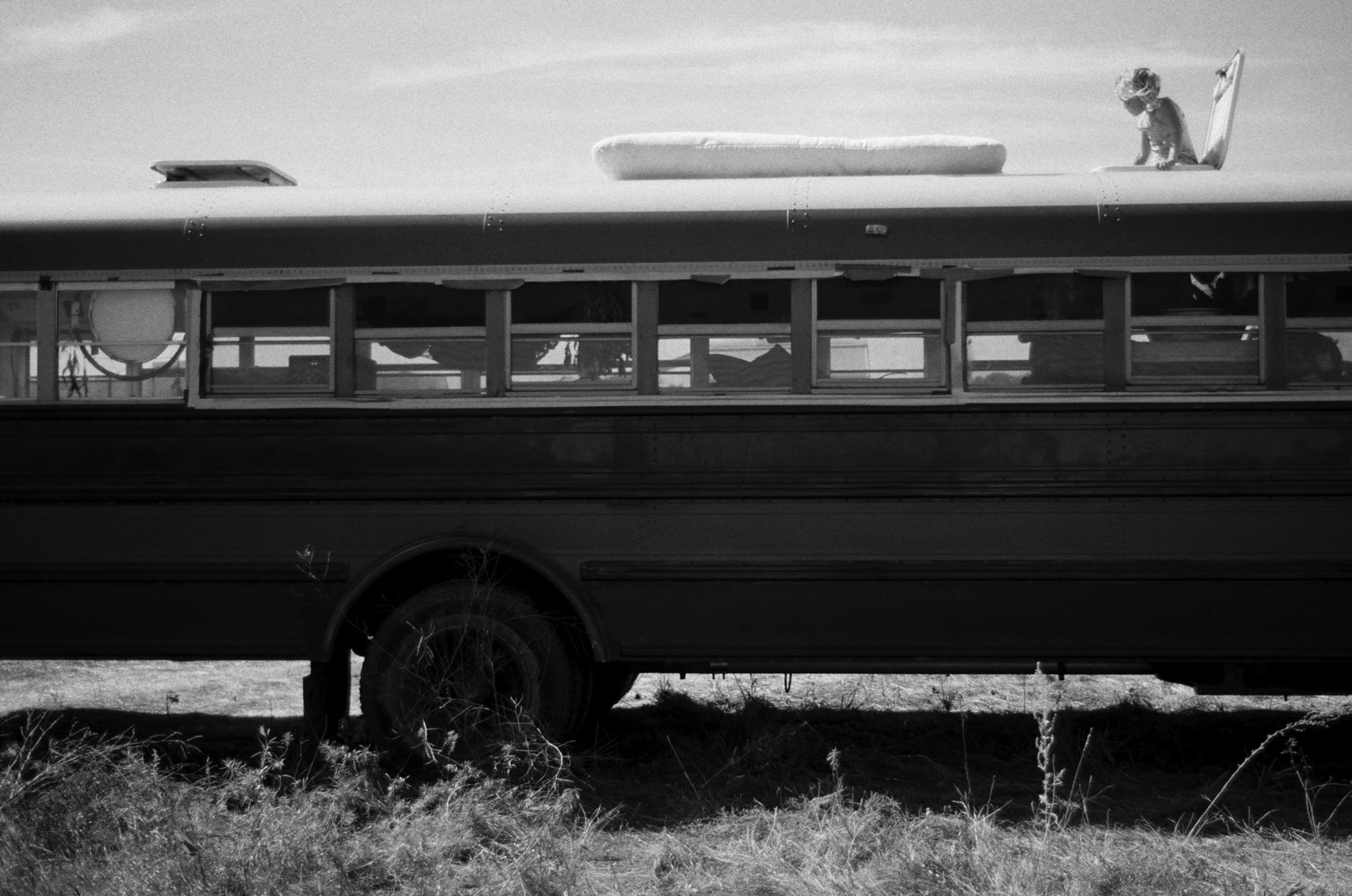 Standing Rock - A young boy leans out of the hatch of an old school bus,...