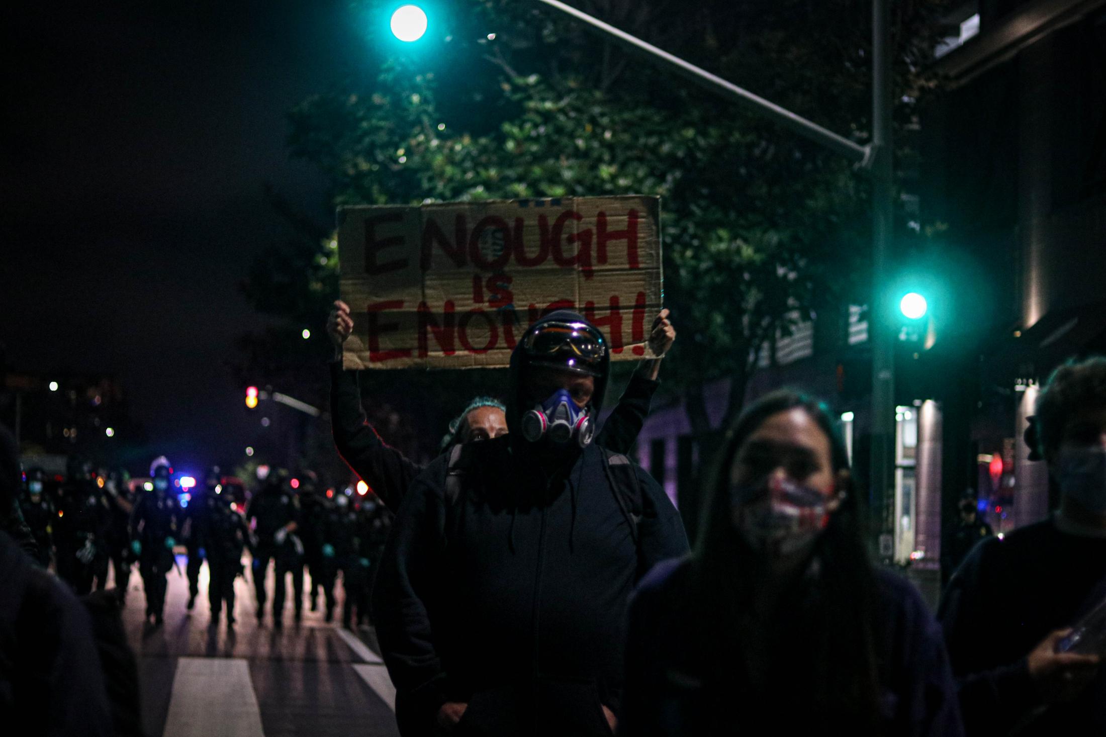 Protests - A protester holds up a sign that says "Enough is...