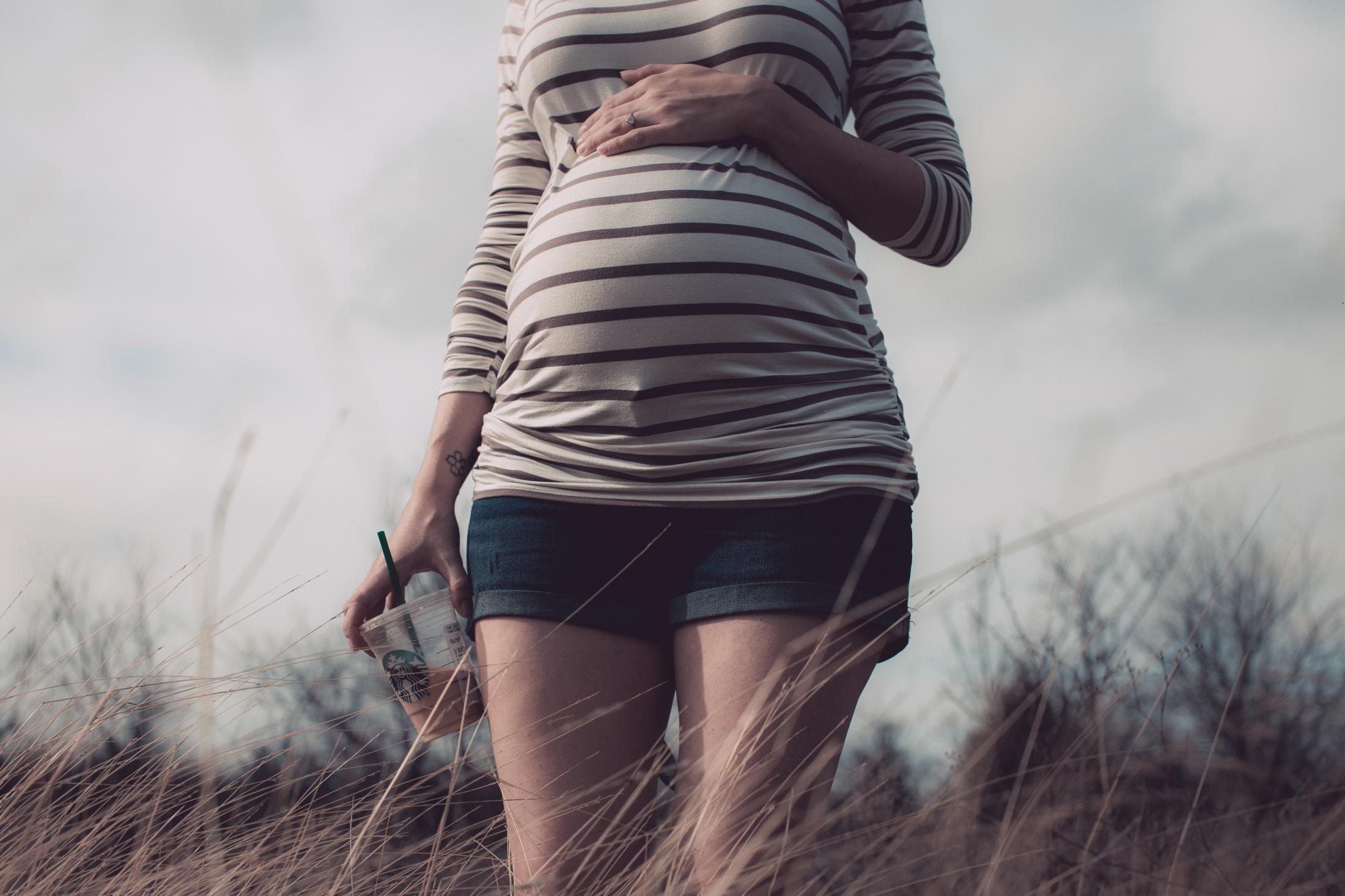 Eight months pregnant, Courtney holds a coffee in her hand during a morning walk in the country.
