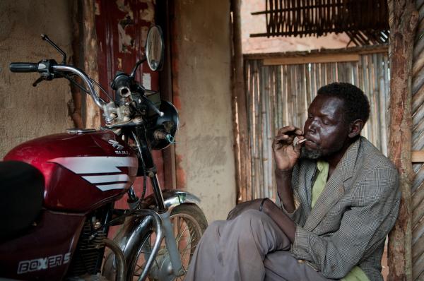 Image from Parenting the Missing - William Oryem smokes a cigarette in a shack close to his...