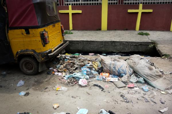 Recycling Lagos  - Uncollected trash is seen next to a tuk-tuk and a gutter....