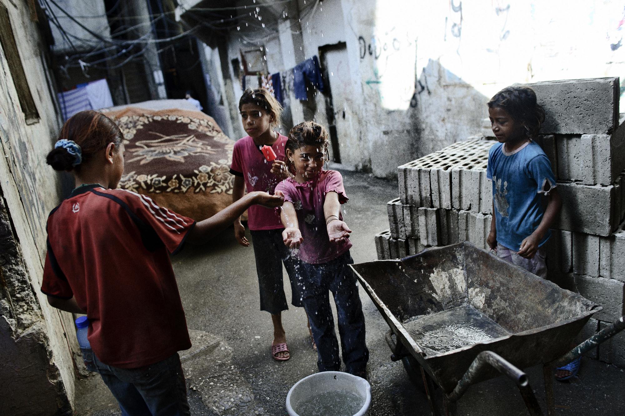 Young Syrian refugees collect water from a leaking water hose in the overcrowded Beirut outskirts Sabra and Shatila in Lebanon, home to refugees...
