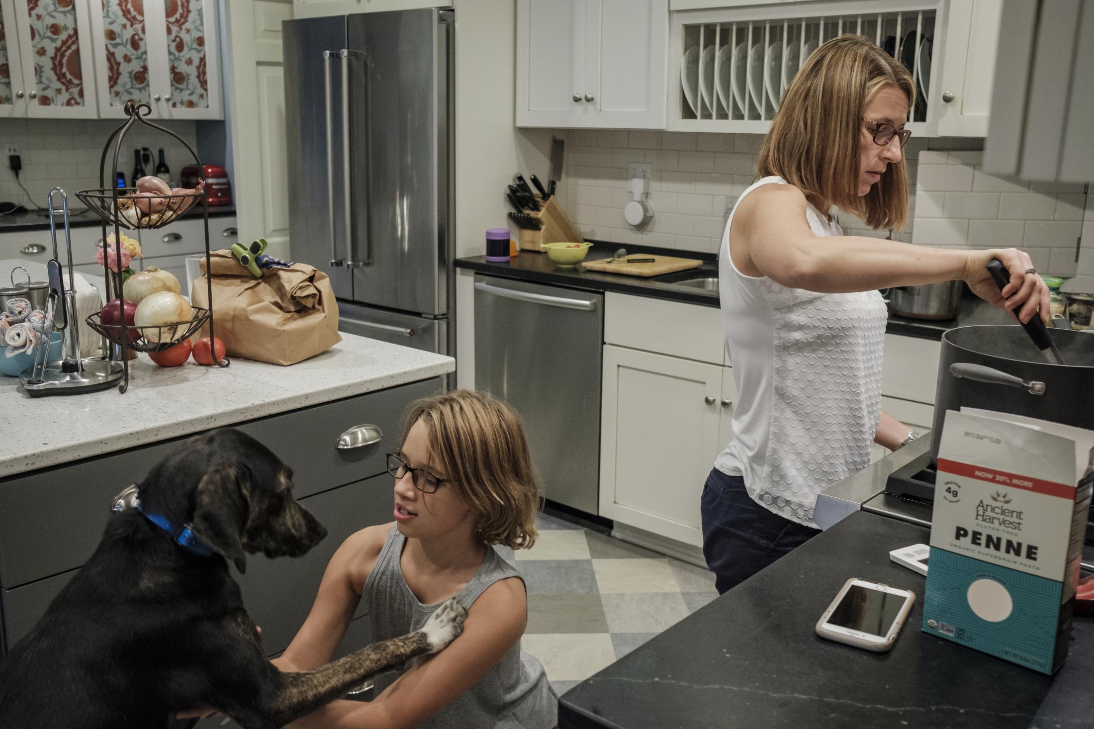 Jeri Seidman cooking dinner while her daughter Hannah plays with her dog Quin at their house in Charlottesville, Virginia, U.S., on Monday Sept. 23, 2019. Hannah is a patient in a genetic risk study about type 1 diabetes at University of Virginia. Photographer: Carlos Bernate/ NPR